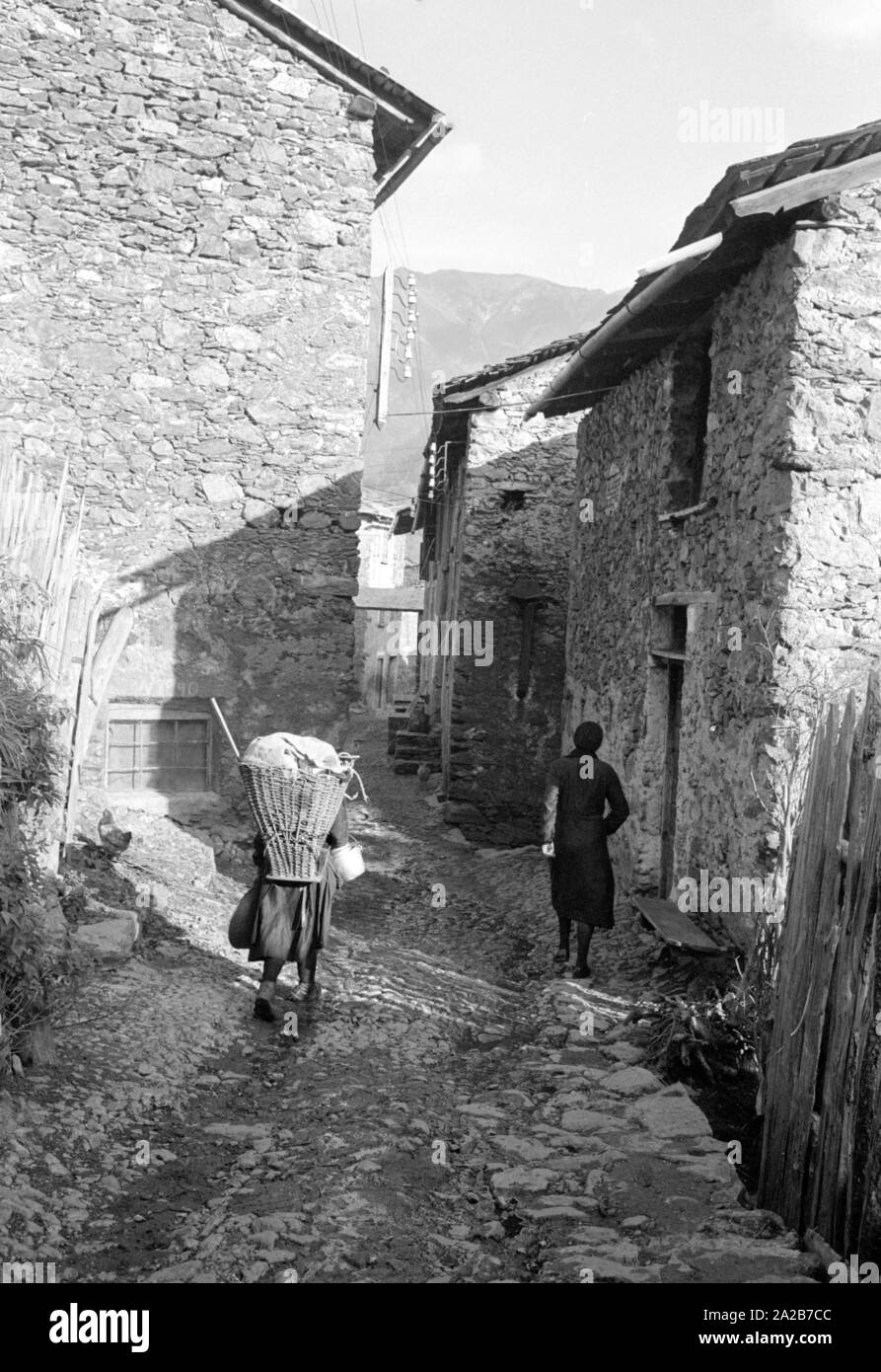 Due donne in un vicolo, la donna sulla sinistra ha un telaio portante. Questa fotografia è stata fatta per la relazione sulla tempesta in Italia. La tempesta ha devastato la città di Loveno, la Valcamonica e Boario Terme in provincia di Brescia in Lombardia. Foto Stock