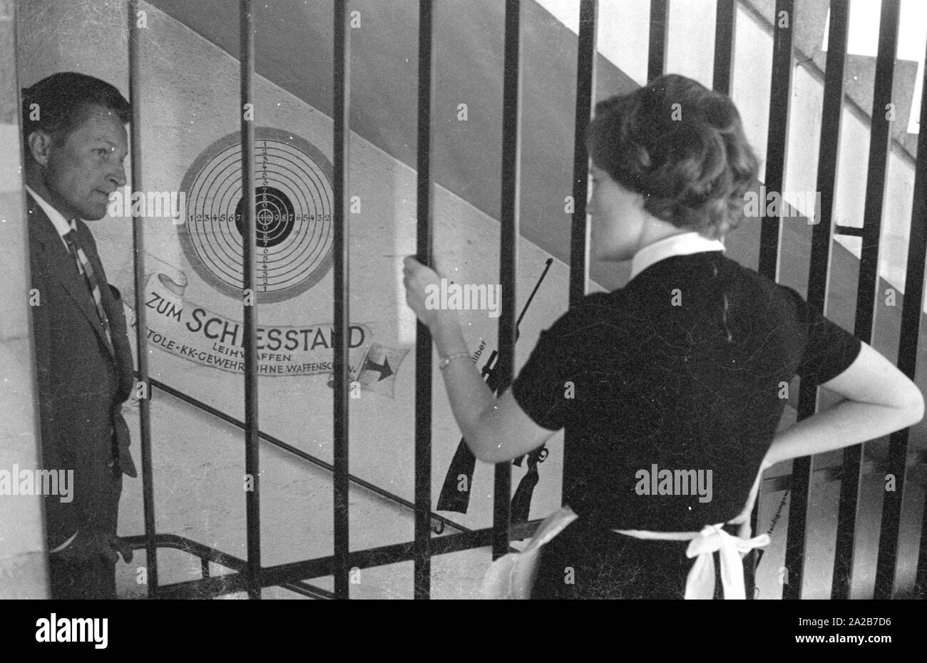Un uomo che indossa una tuta parla di una donna come egli cammina giù per le scale per il tiro a segno. Il 'Pistolen-Club-Baviera e.V. " è stata fondata il 7 novembre 1961, e nei primi anni di operato in un poligono di tiro nel seminterrato del complesso Mathaeser, non lontano da Stachus a Monaco di Baviera. Foto non datata, probabilmente negli anni sessanta. Foto Stock