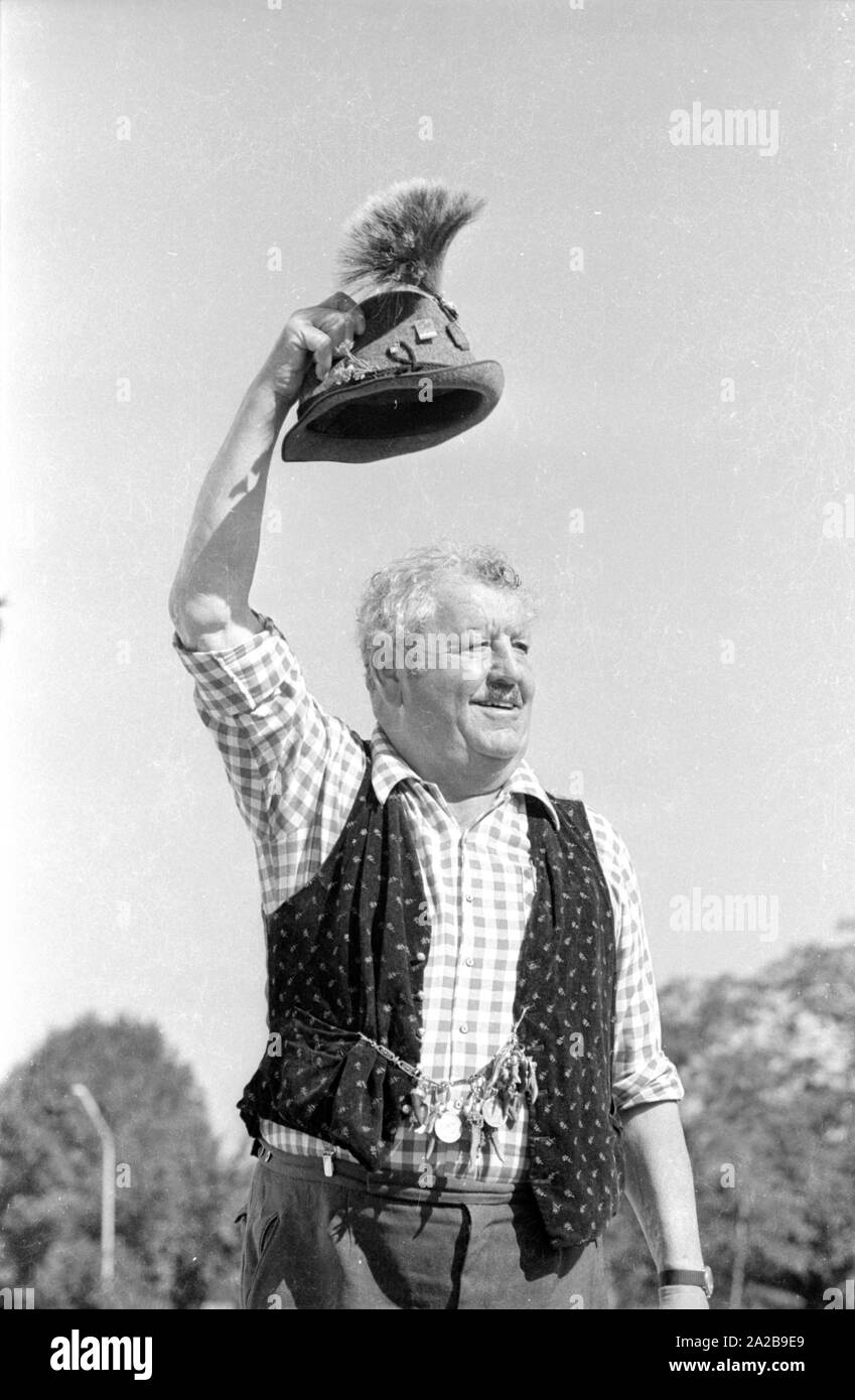 Un uomo in abiti tradizionali solleva il suo cappello nel messaggio di saluto. Foto Stock