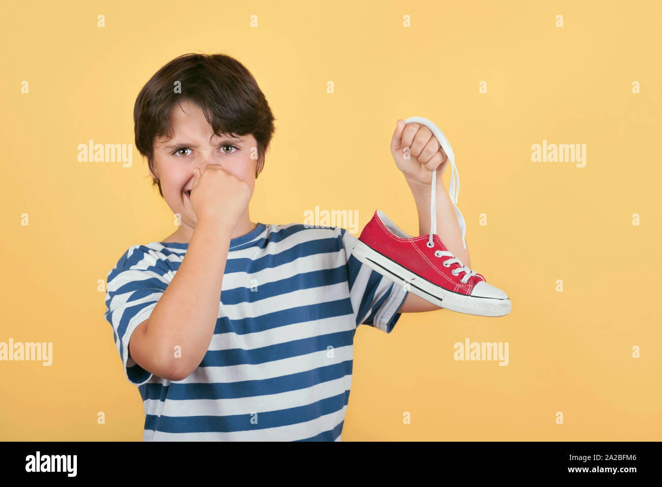 Bambino azienda puzzolenti sneakers scarpe su sfondo giallo Foto Stock