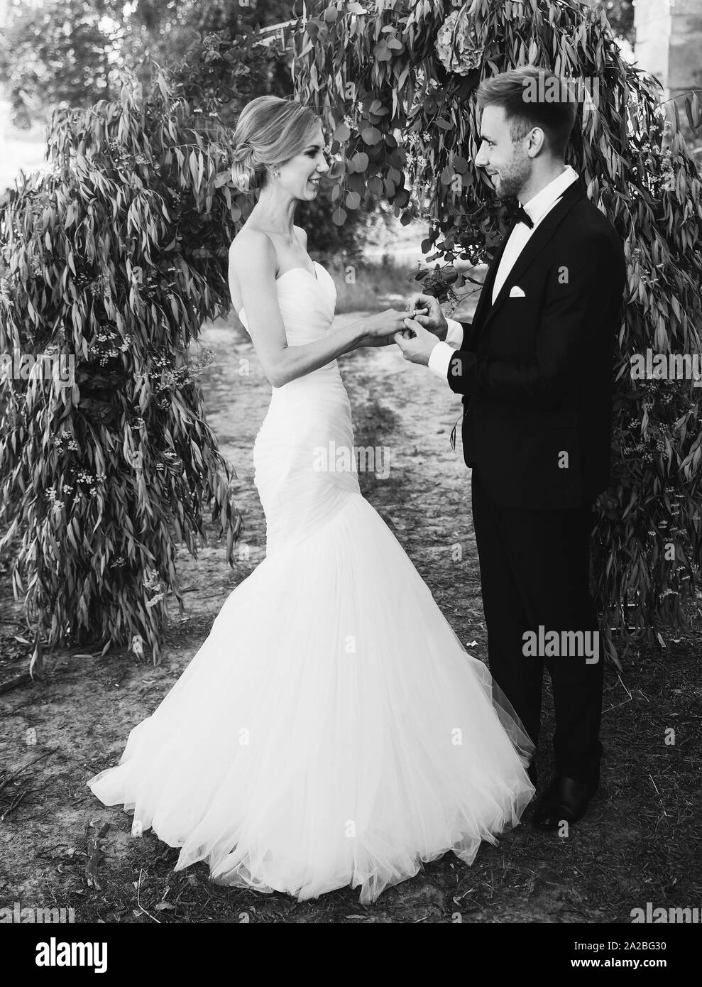 Matura in un abito da sposa anelli di scambi in giardino con un arco. foto in bianco e nero Foto Stock