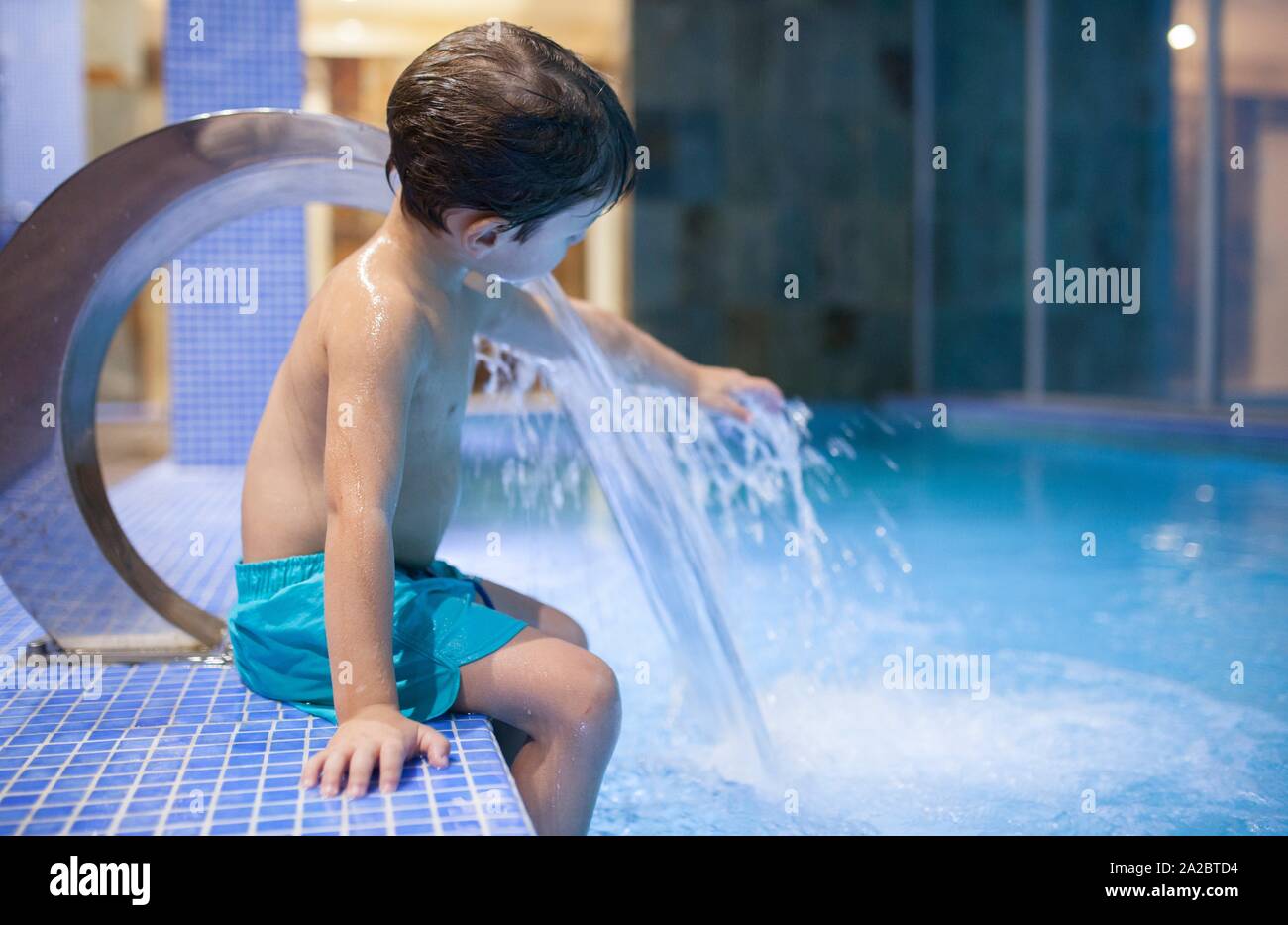 4 anni ragazzo giocando con getti a piscina coperta termale. Messa a fuoco selettiva. Foto Stock