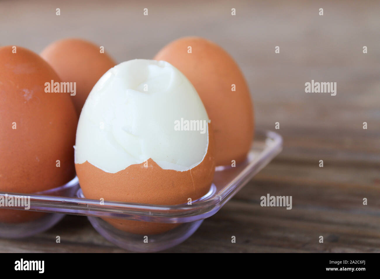 Chiudere fino a sei uova di colore marrone in scatola di plastica sul tavolo di bambù con uno rotto uova sode. Foto Stock