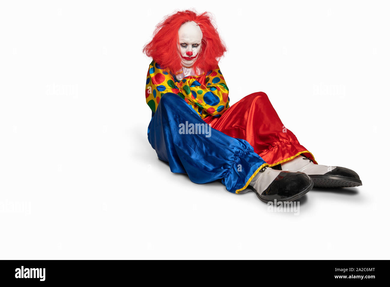 Triste clown seduto sul pavimento isolato sullo sfondo Foto Stock