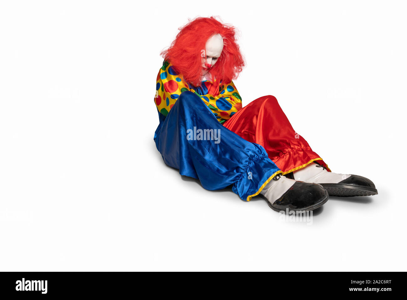 Triste clown è seduta sul pavimento guardando verso il basso Foto Stock