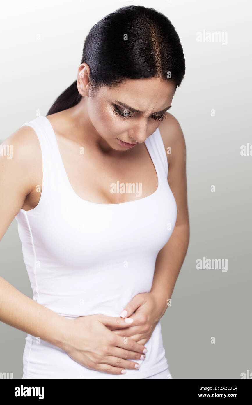 Donna del dolore. Ferite da un doloroso stomaco, tenendo le mani sullo stomaco. Problemi di salute, il concetto di salute. Bella giovane donna. Su un livello di grigio Foto Stock