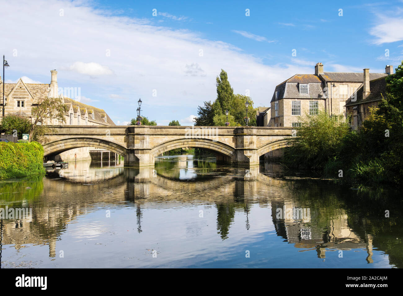 Acqua calma riflettente edifici di pietra calcarea e il ponte di pietra sul fiume Welland visto dai prati park. Stamford Lincolnshire England Regno Unito Gran Bretagna Foto Stock