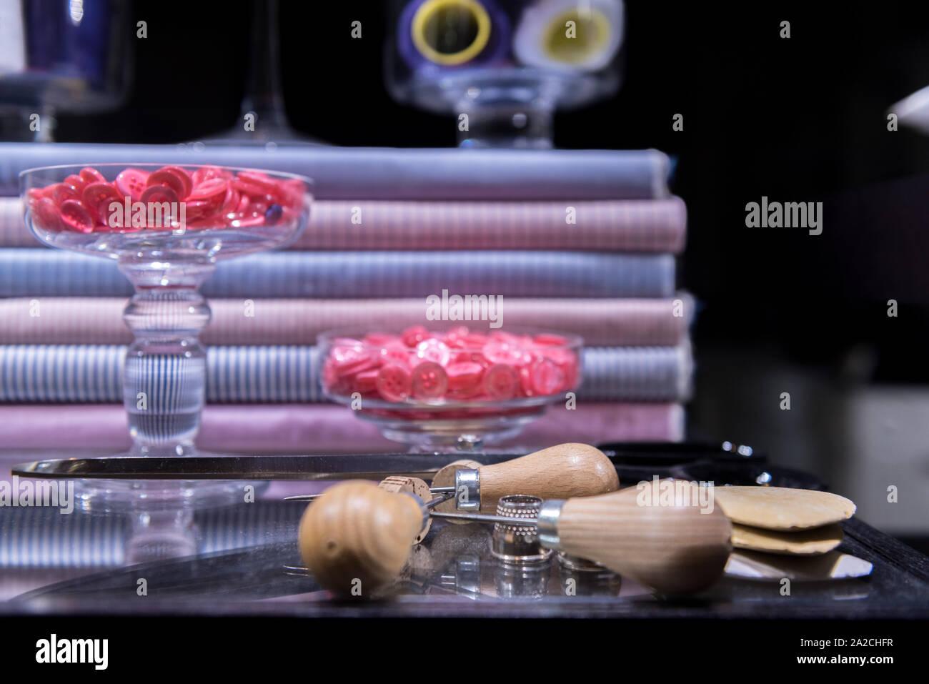 Sartoriale forbici, AWL, gesso e ditale presentata sul tavolo di vetro circondato da pulsanti e tessuto della camicia Foto Stock