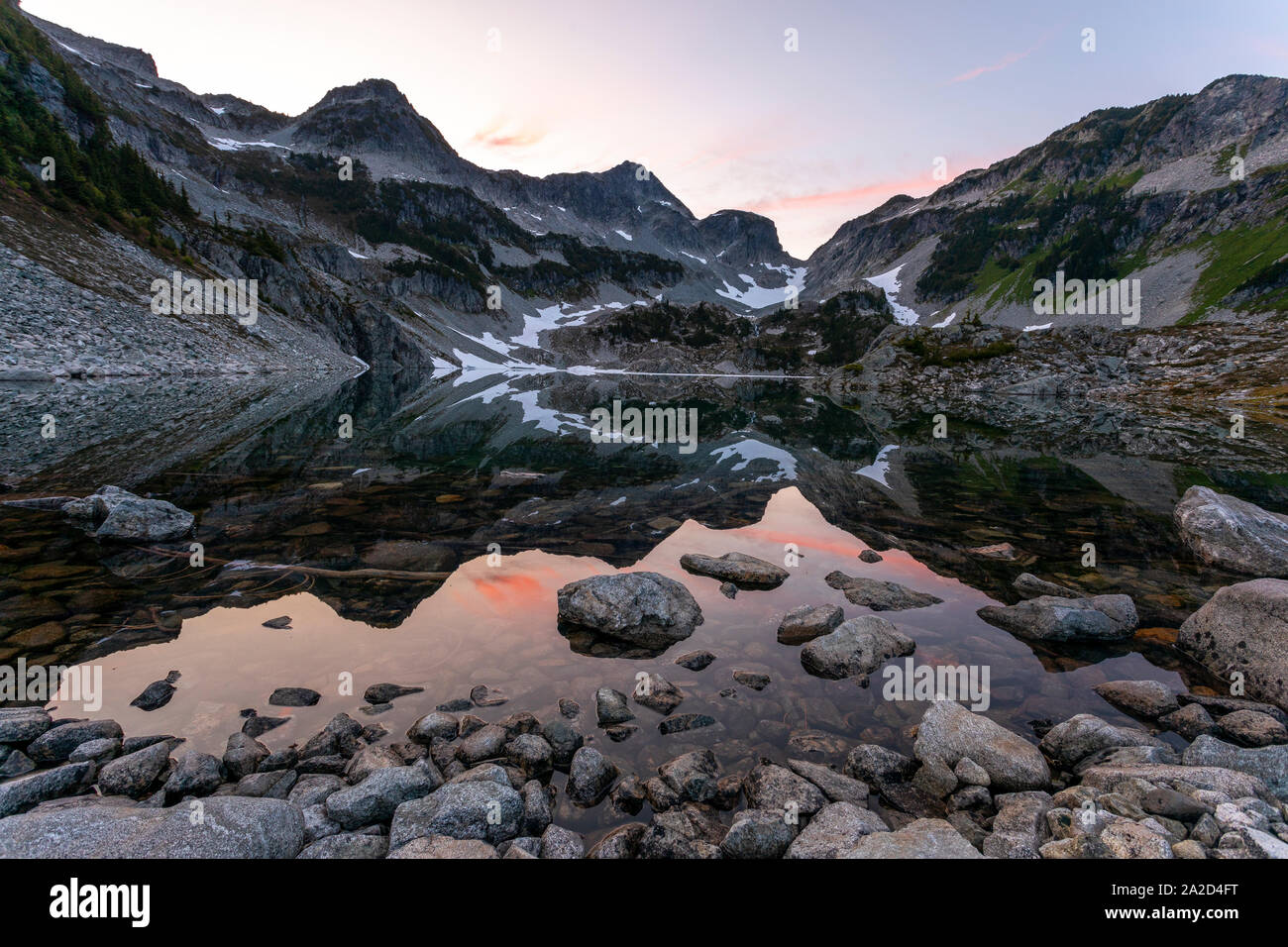 Il sole tramonta su un lago alpino circondato da vette. Foto Stock