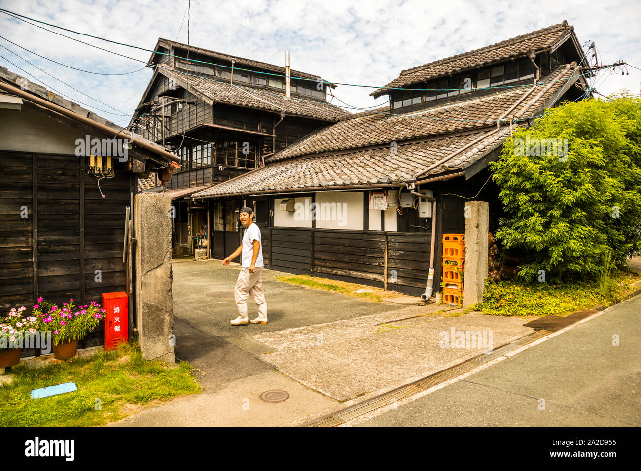 Un membro dello staff attraversa il cortile della manifattura di salsa di soia Meijiya, in attività a Hamamatsu, Giappone, dal 1872, il suo edificio in legno di cedro a tre piani risale alla sua fondazione. Foto Stock