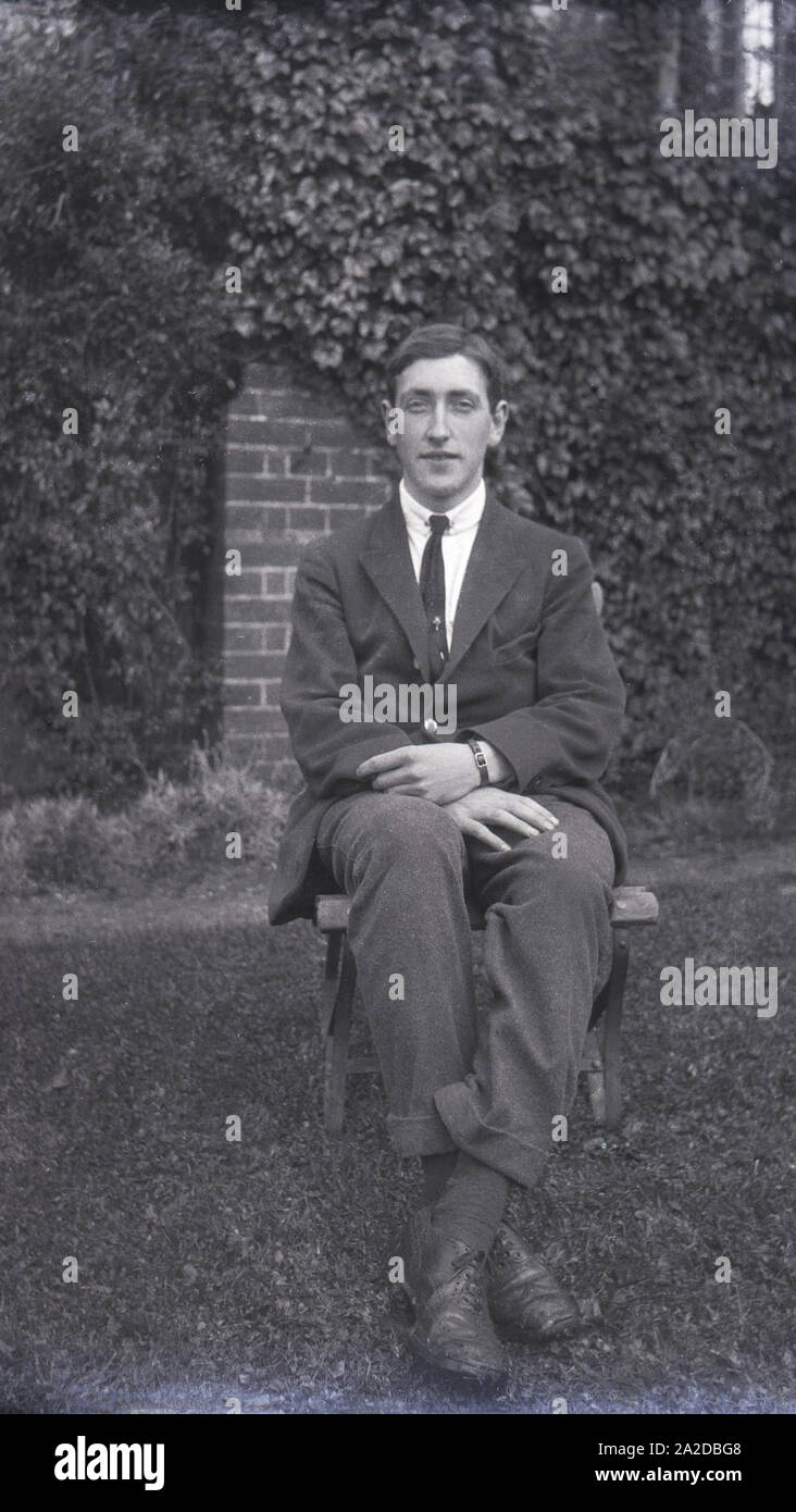 1920s, storico, un giovane uomo in giacca e cravatta seduto in una piccola  sedia di legno in un giardino, Inghilterra Foto stock - Alamy