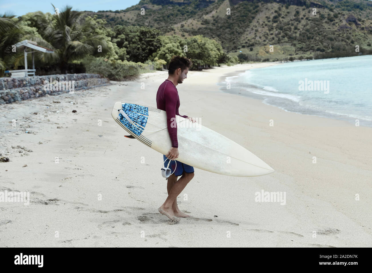 Giovane uomo con la tavola da surf in spiaggia Foto Stock