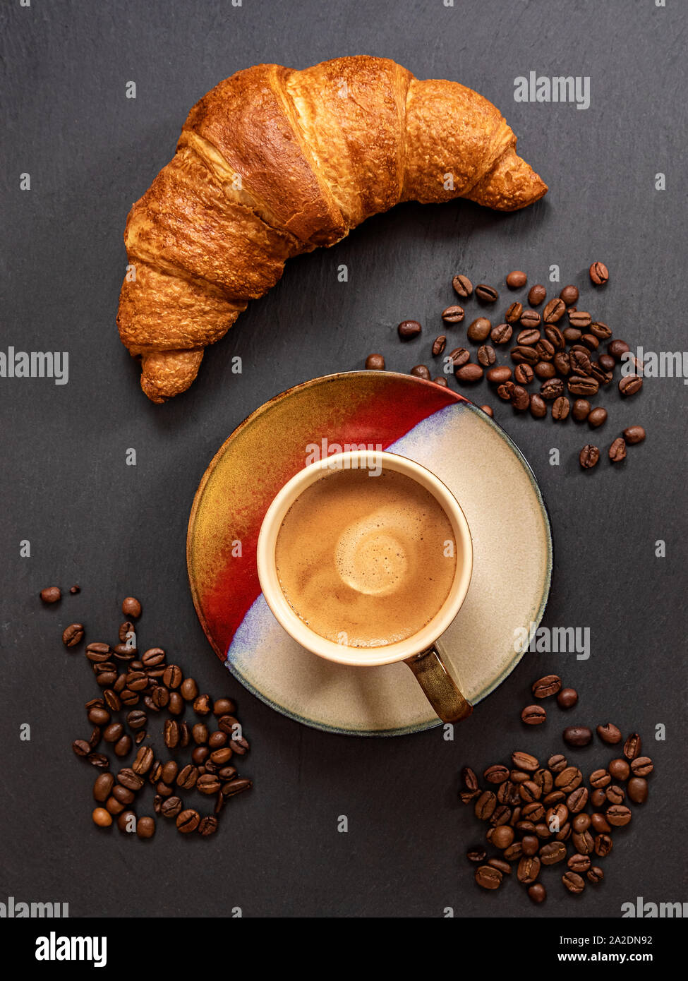 Tazza da caffè con croissant francesi e i chicchi di caffè su grigio ardesia sfondo. Vista dall'alto. Foto Stock