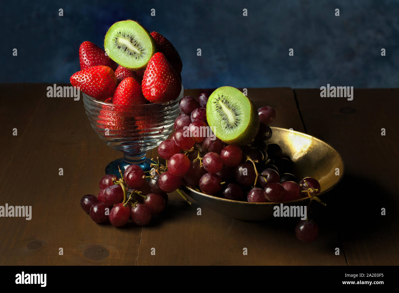 Uva su una ciotola con metà kiwi sulla parte superiore e una tazza con fragole su di essa con una metà di kiwi sulle fragole Foto Stock
