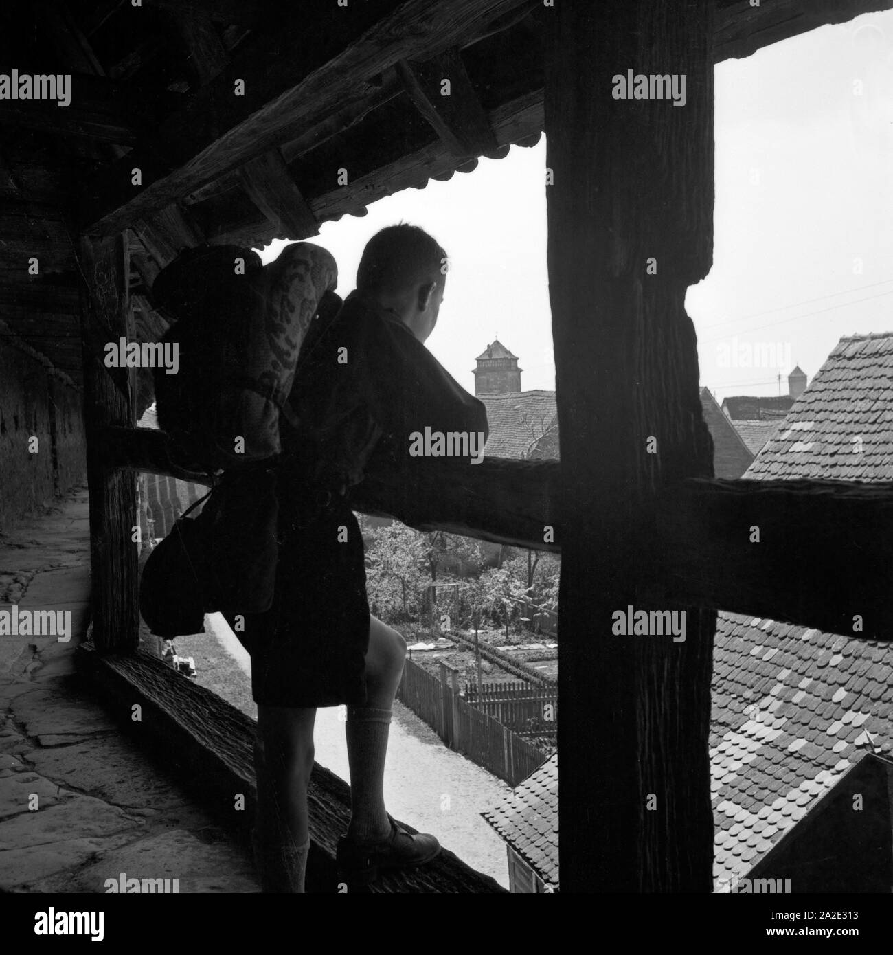 Ein Hitlerjunge schaut auf einer Wanderung aus einem Turmfenster auf eine Altstadt, Deutschland 1930er Jahre. Una gioventù hitleriana guardando da un watchout a una vecchia città, Germania 1930s. Foto Stock