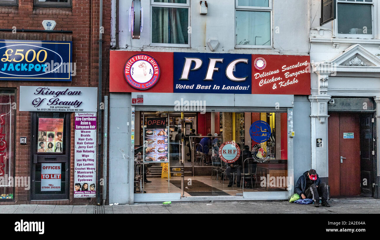Perfetto il pollo fritto. Negozio di pollo con senzatetto uomo seduto all'esterno. West Bromwich, West Midlands, Regno Unito. Foto Stock