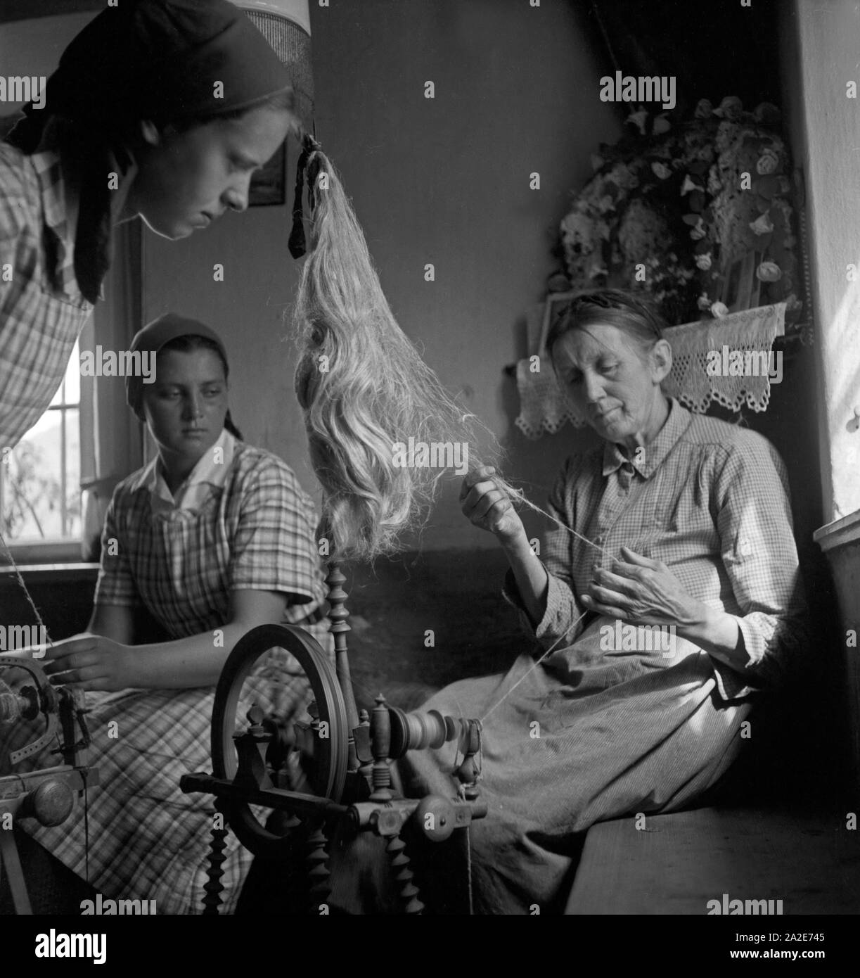 Eine alte Frau zeigt zwei jungen Mädchen das Arbeiten mit dem Spinnrad in Hohenaschau im Chiemgau, Deutschland 1930er Jahre. Una donna anziana che mostra per giovani ragazze come lavorare con una ruota di filatura a Hohenaschau, Germania 1930s. Foto Stock