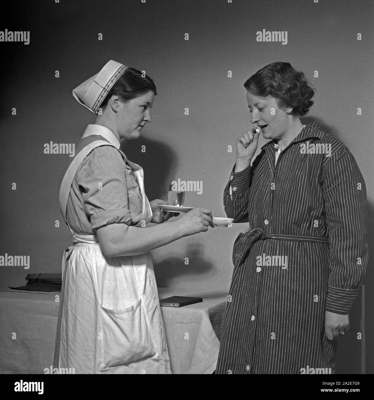 Eine junge Schwester des Deutschen Roten Kreuzes verarbreicht einer Kranken eine Tablette, Deutschland 1930er Jahre. Un giovane infermiere della Croce Rossa tedesca applicando una pillola per una donna malata, Germania 1930s. Foto Stock