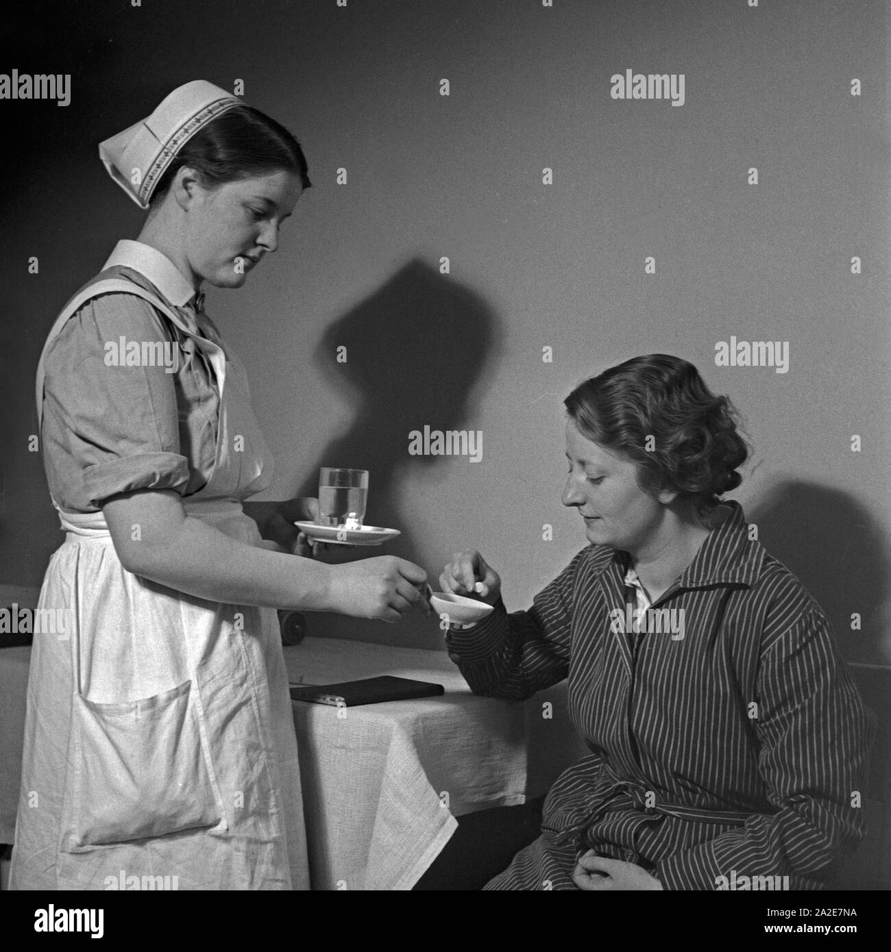 Eine junge Schwester des Deutschen Roten Kreuzes verarbreicht einer Kranken eine Tablette, Deutschland 1930er Jahre. Un giovane infermiere della Croce Rossa tedesca applicando una pillola per una donna malata, Germania 1930s. Foto Stock