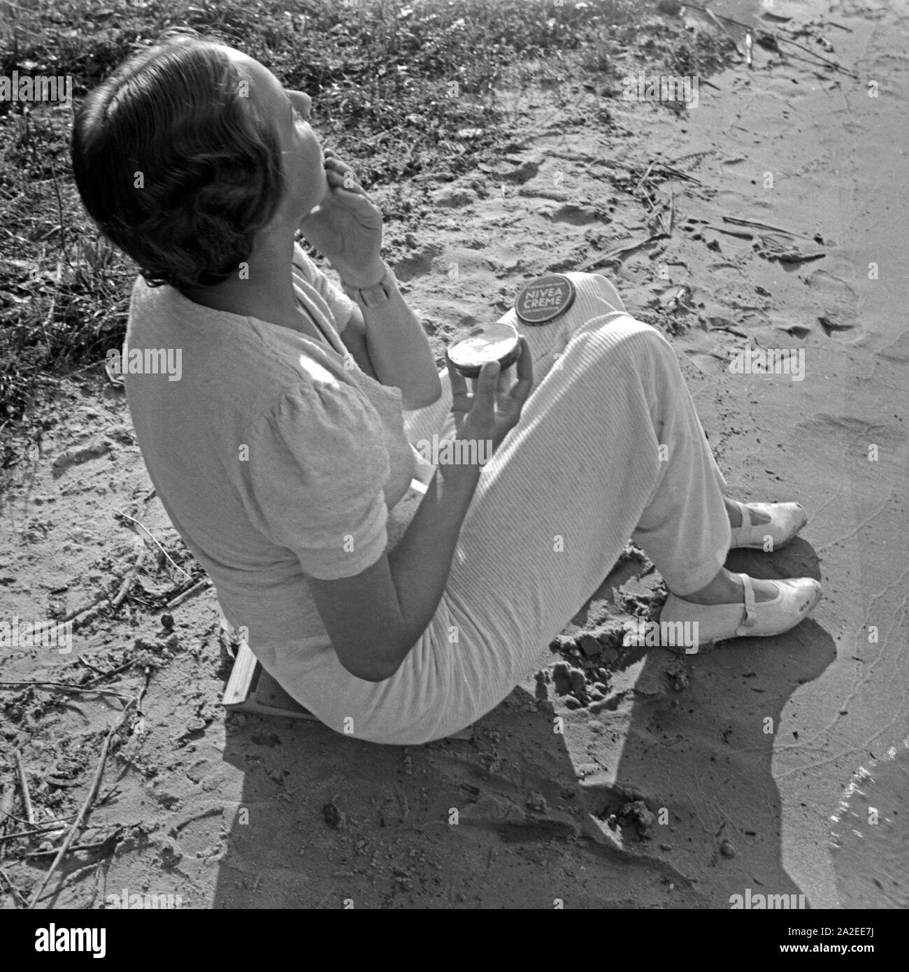 Einen guten Schutz gegen Sonnenbrand bietet crema Nivea, eine junge Frau am Ufer eines vede , Deutschland 1930er Jahre. Una crema Nivea protegge le scottature, giovane donna creaming, Germania 1930s. Foto Stock