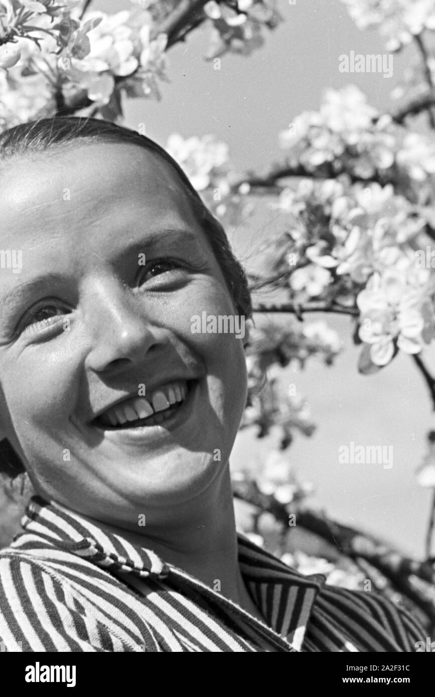 Eine junge Frau unter einem blühenden Kirschbaum im Schwarzwald, Deutschland 1930er Jahre. Una giovane donna sotto una fioritura di ciliegio nella Foresta Nera, Germania 1930s. Foto Stock