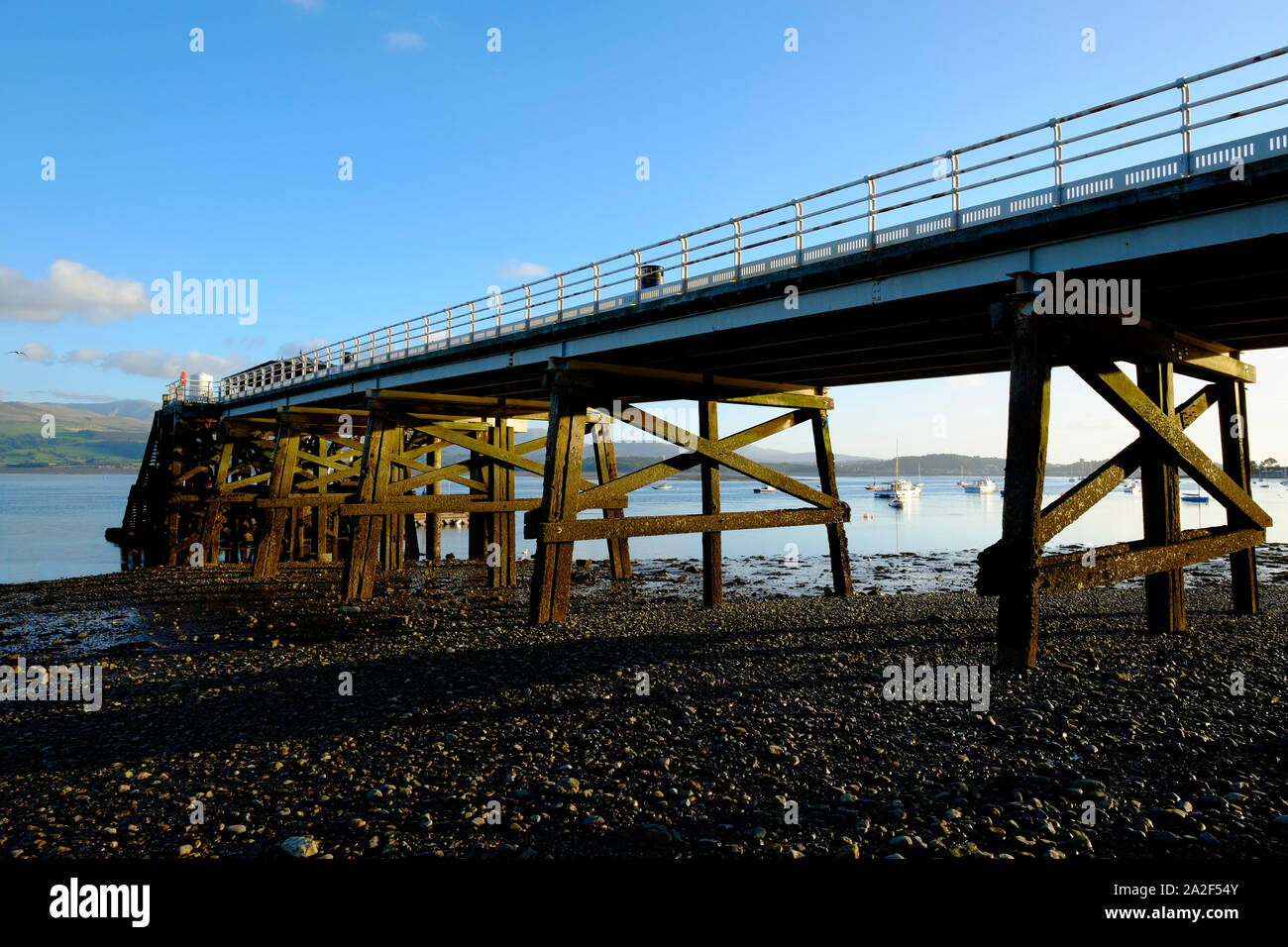 Una vista in Beaumaris Pier mostra i supporti in legno sottostruttura con la bassa marea in serata sole Foto Stock