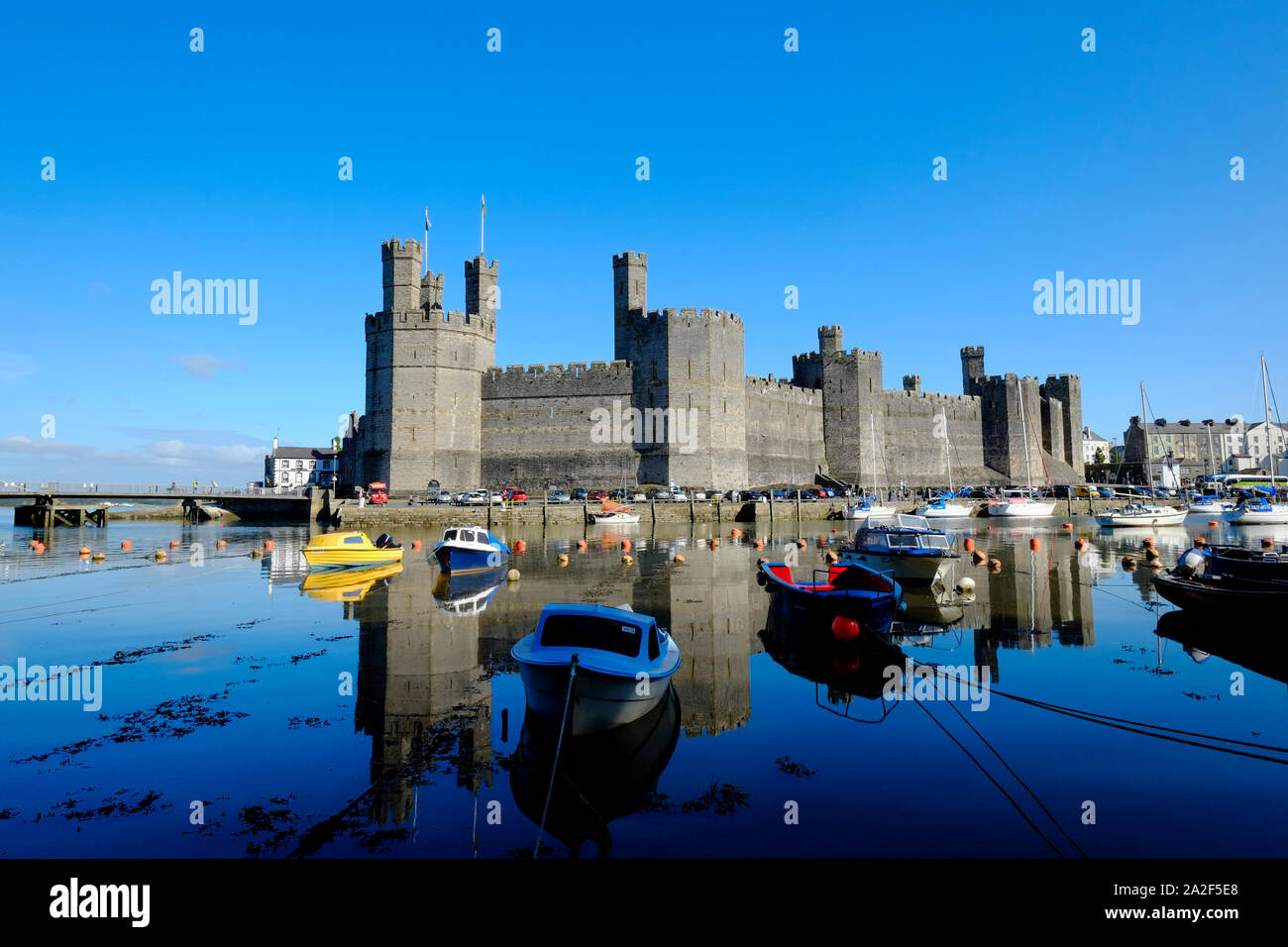 Vista sul Fiume Sieont verso Caernarfon Castle su ancora un calmo mattino riflettendo sull'acqua ad alta marea con barche ormeggiate in primo piano Foto Stock