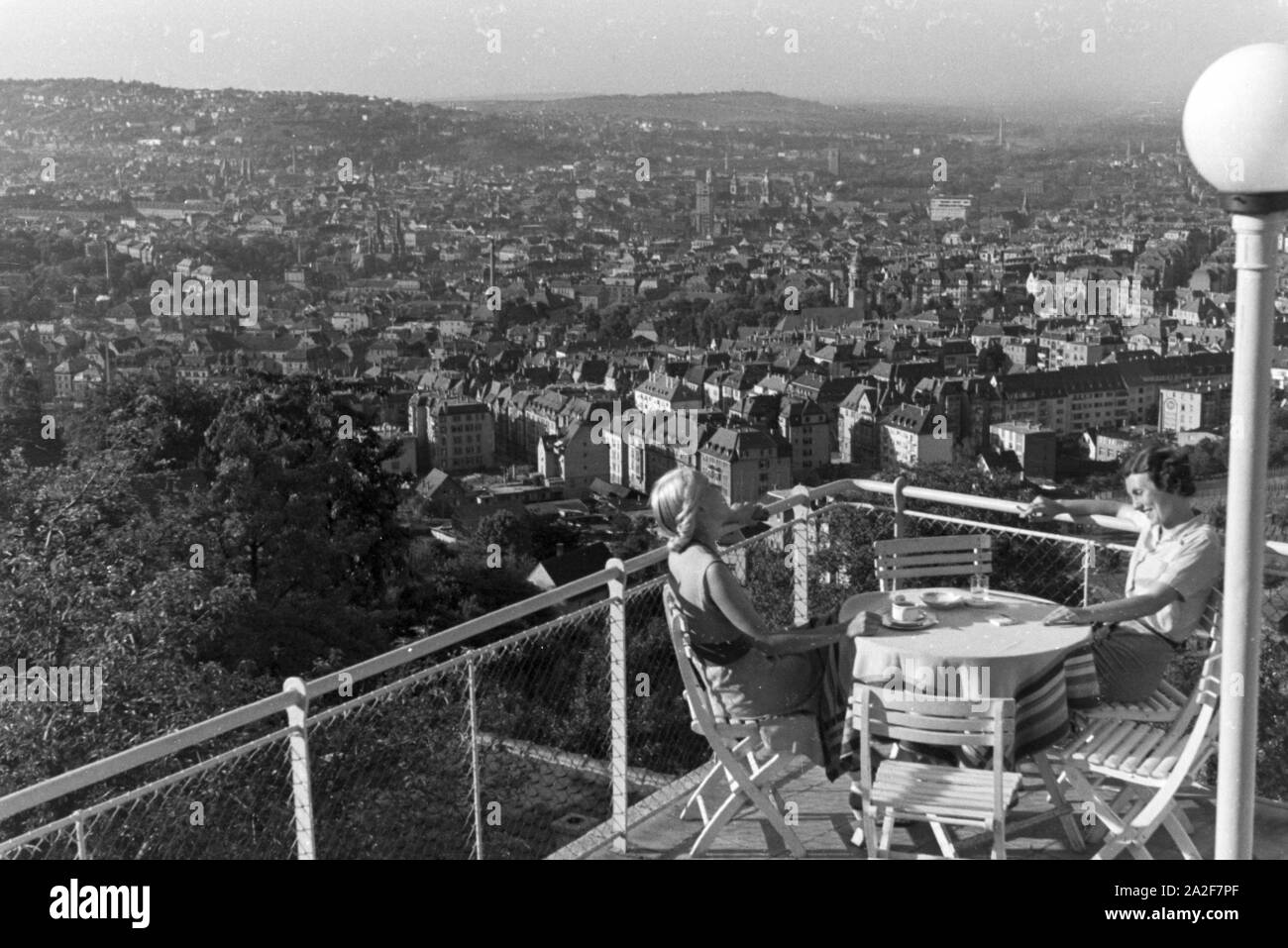 Zwei junge Frauen genießen von der Caféterrasse aus den Blick über Stuttgart, Deutschland 1930er Jahre. Due giovani donne godono della vista su Stoccarda dalla terrazza di un caffè, Germania 1930s. Foto Stock