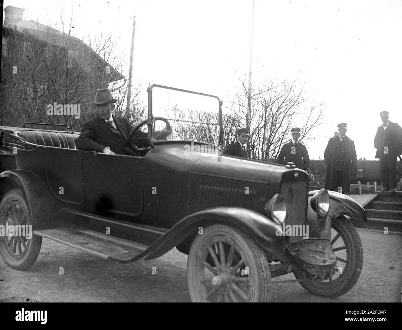 En uomo sitter i en bil järnväg invid. Fyra uniformsklädda män ho bakgrunden - Foto Stock