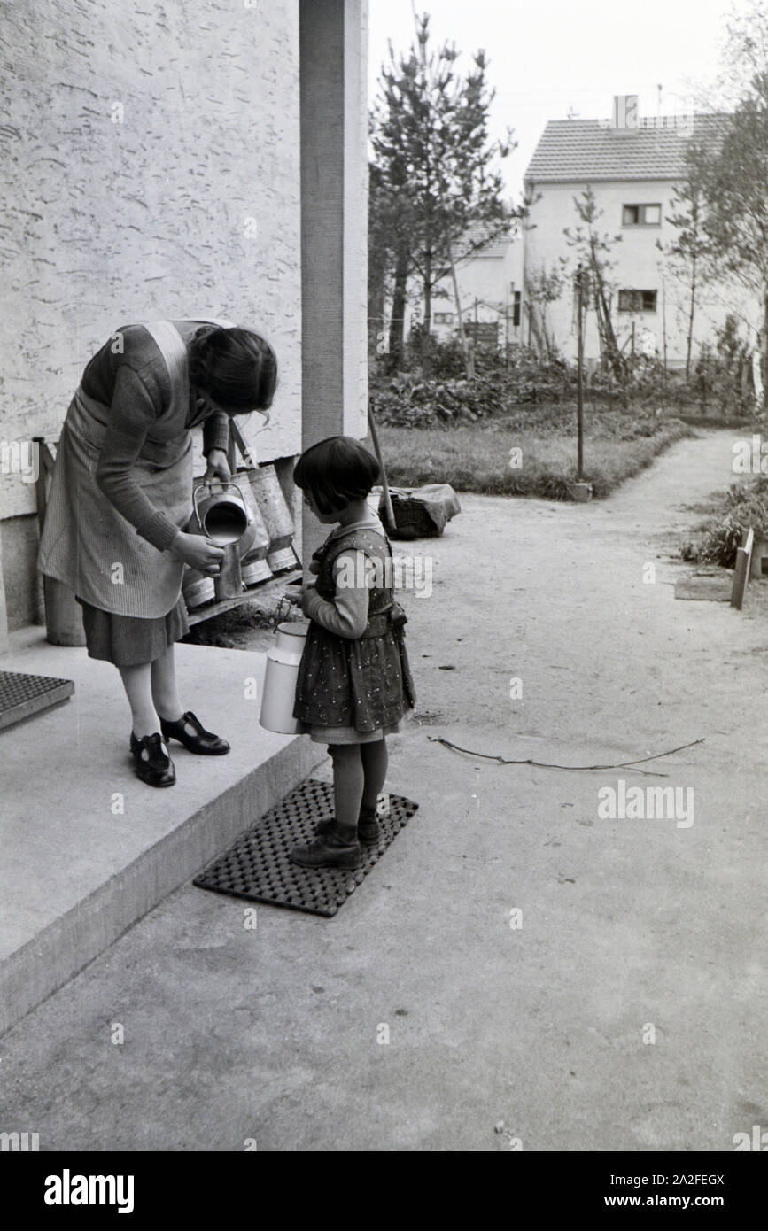 Eine Frau füllt einem kleinen Mädchen einen beker Milch aus einer großen Milchkanne ab, Zeppelinsiedlung bei Frankfurt am Main, Deutschland 1930er Jahre. Una donna si riempie una tazza con il latte al di fuori di un grande latte può per una bambina, zeppelin villaggio nei pressi di Frankfurt am Main, Germania 1930s. Foto Stock