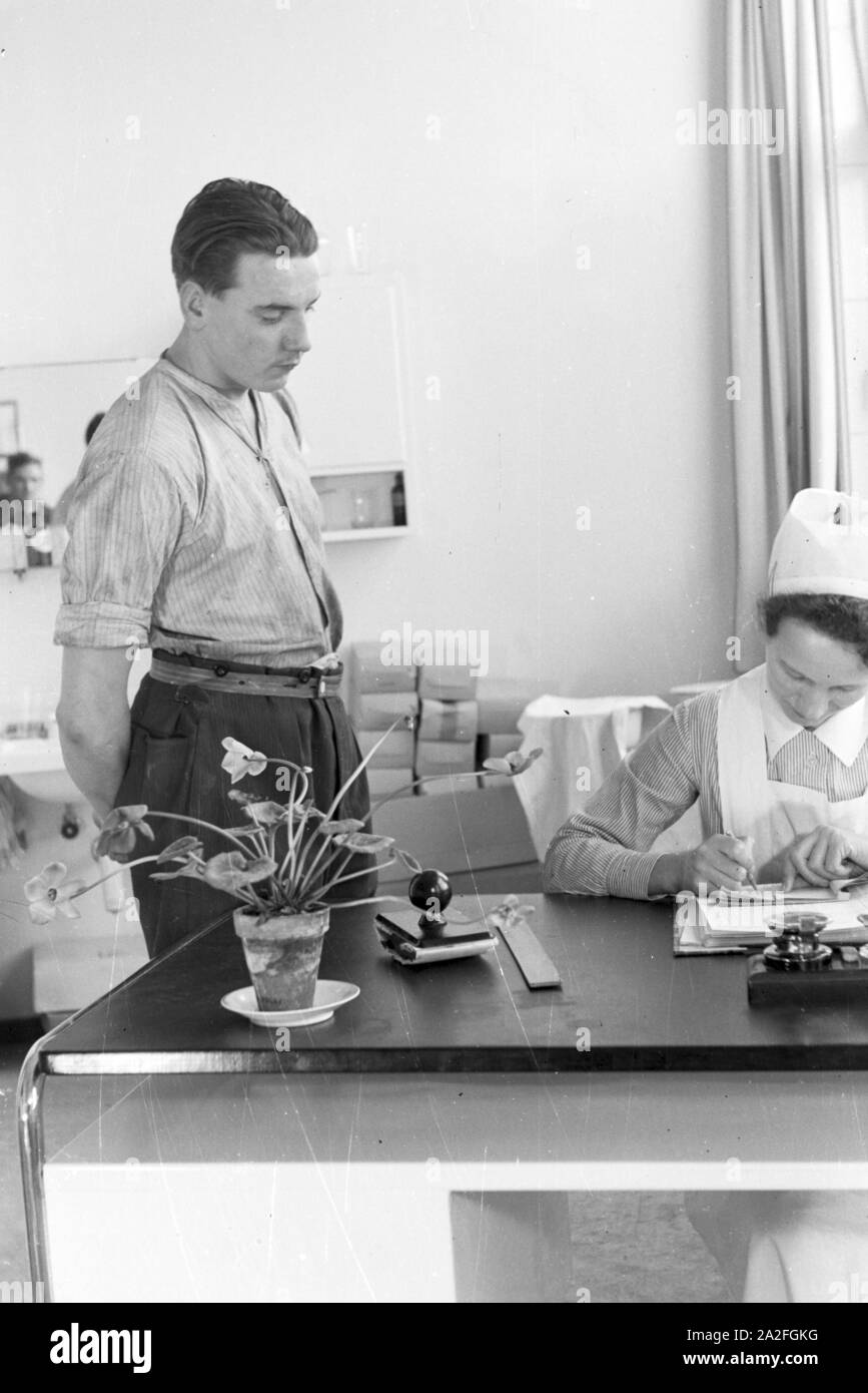 Eine Krankenschwester schreibt einem jungen Mann ein Rezept, Deutschland 1930er Jahre. Un infermiere è la scrittura di una ricetta per un uomo giovane, Germania 1930s. Foto Stock