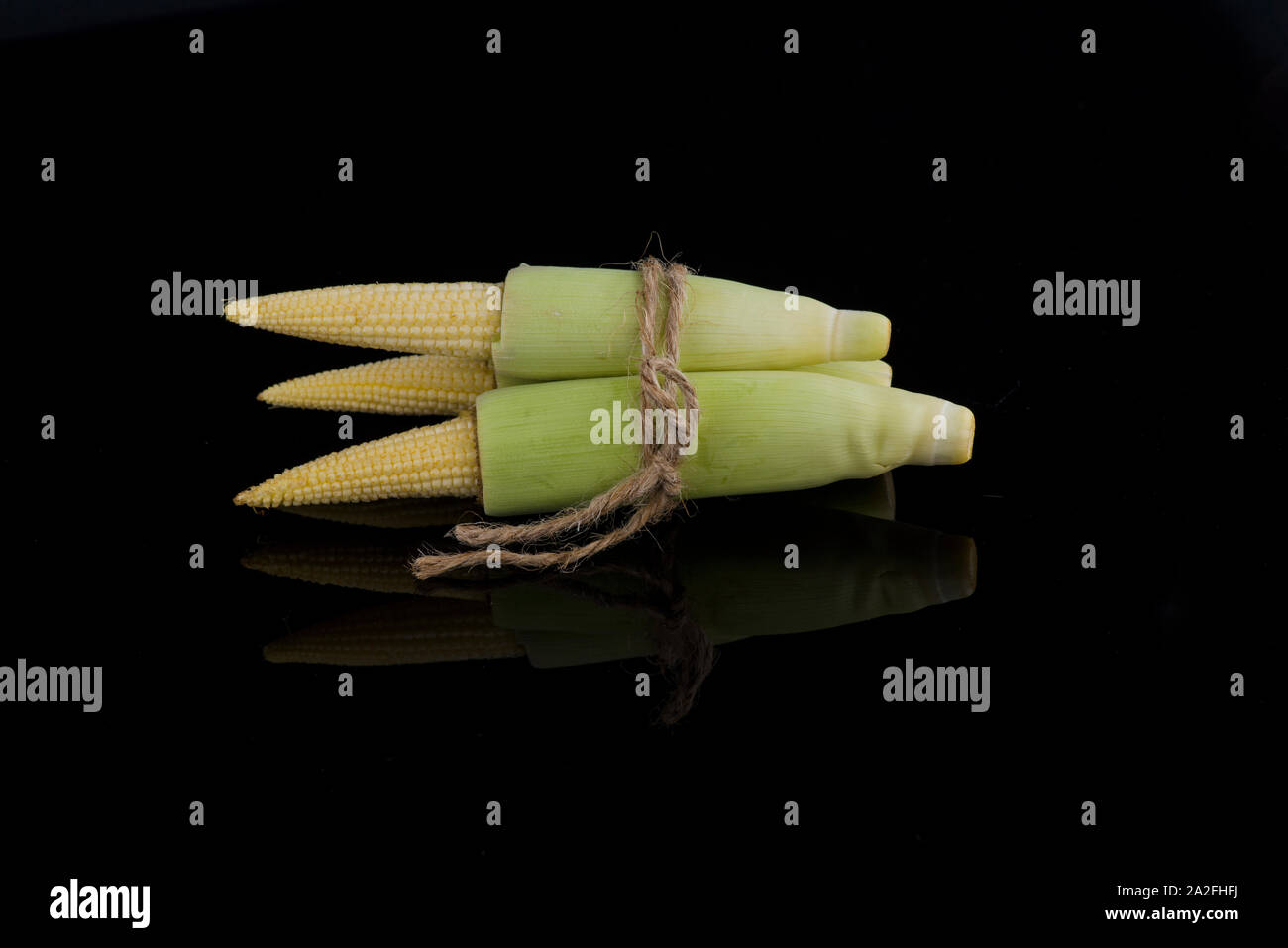 Giovani materie baby corn isolati su sfondo nero con una piccola riflessione Foto Stock