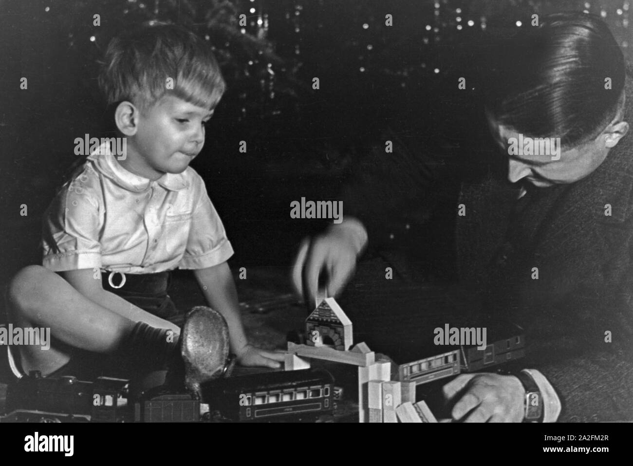 Typisches Weihnachtsbild: Der kleine Sohn bekommt eine Eisenbahn geschenkt und der Vater spielt damit, Deutschland 1930er Jahre. tipico Natale foto: un ragazzino ottiene un trenino e suo padre è giocare con essa, Germania 1930s. Foto Stock