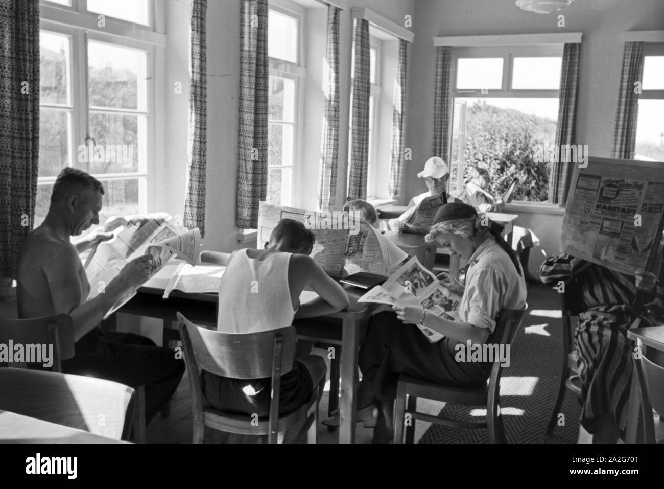 In einem Wartesaal lesen wartende Reisende die aktuellen Meldungen aus der Tageszeitung, Deutschland 1930er Jahre. In attesa di passeggeri leggendo i quotidiani in una sala di attesa di una stazione principale, Germania 1930s. Foto Stock