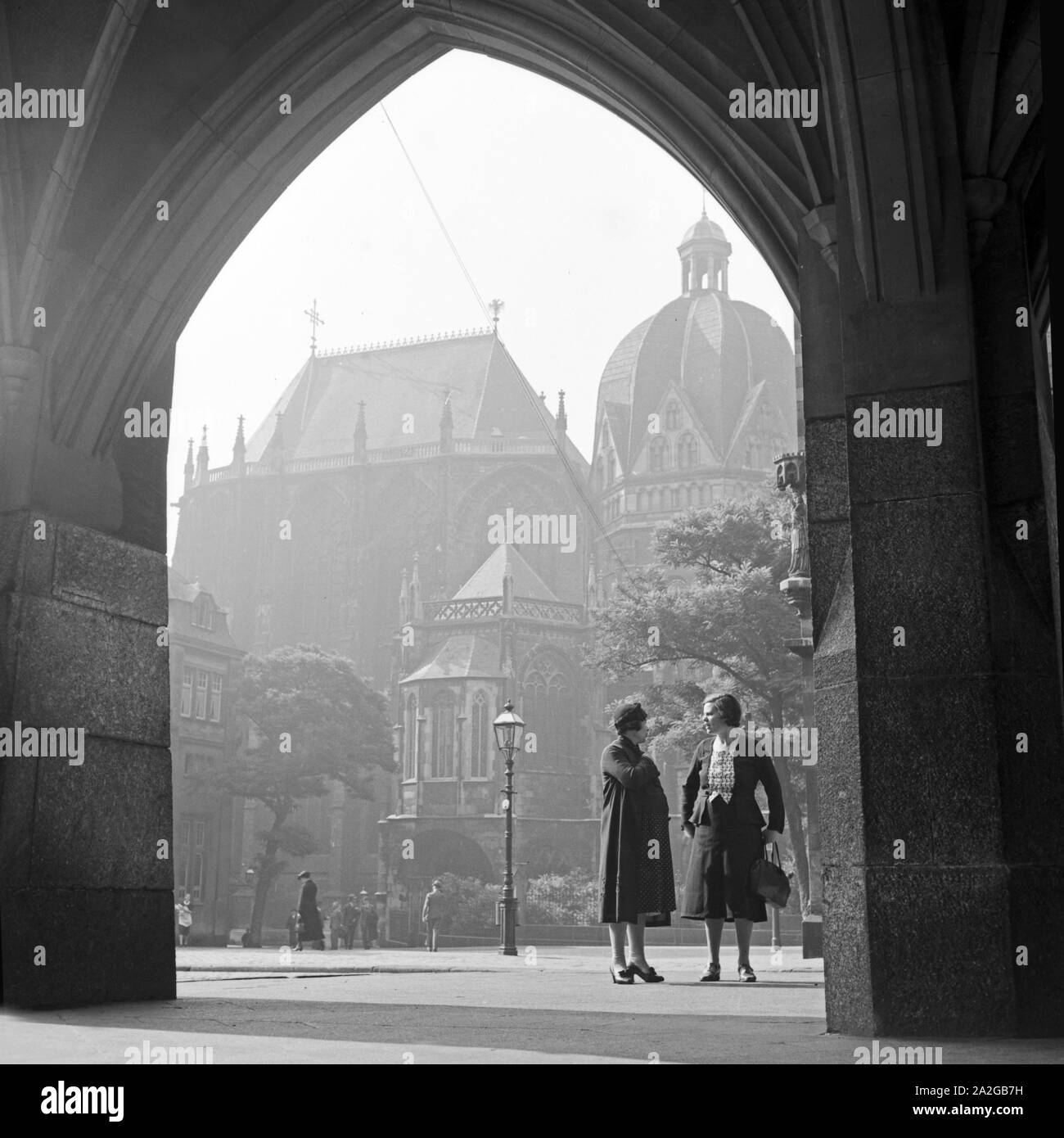 Zwei Frauen unterhalten sich im Kolonnadengang des Rathauses am Katschhof in Aachen mit dem Kaiserdom in Hintergrund, Deutschland 1930er Jahre. Due donne in chat con i colonnati archway dello stile barocco al municipio di Aachen con la cattedrale in background, Germania 1930s. Foto Stock