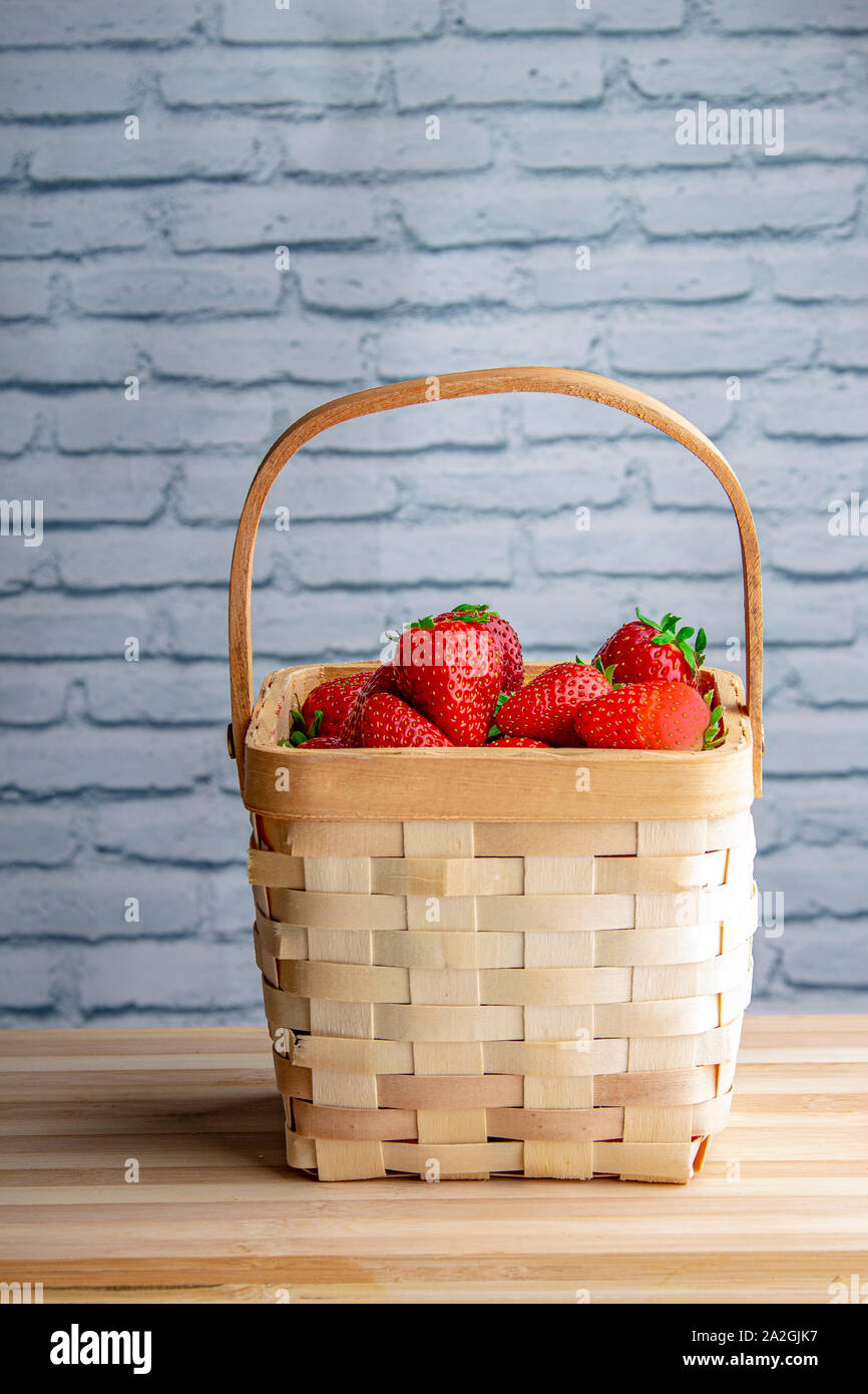 Le fragole in un cestello di legno e un tavolo di legno con un bianco muro di mattoni Foto Stock