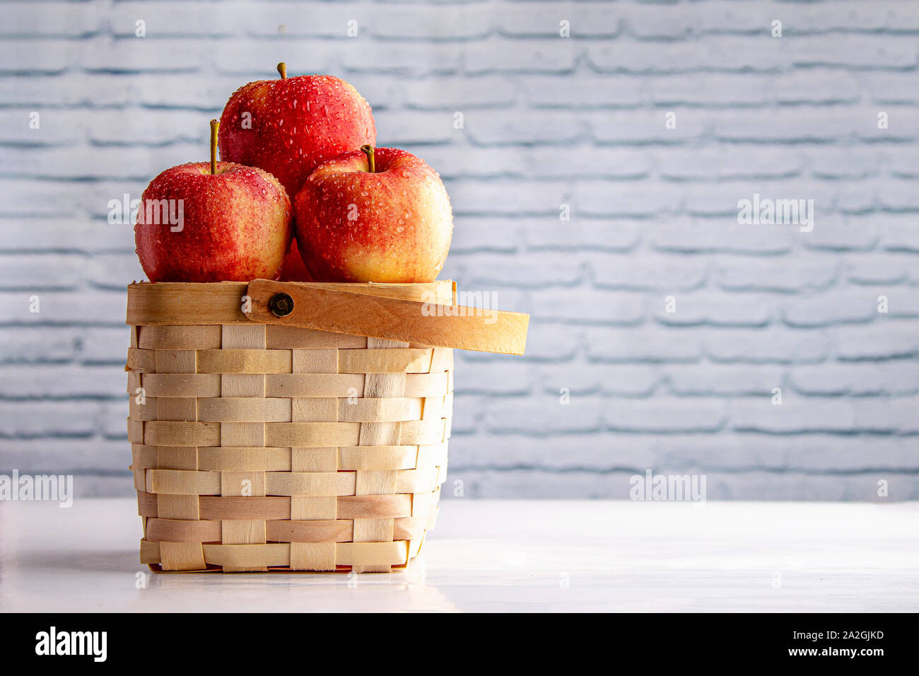 Le mele su un cestello di legno su un tavolo bianco con un bianco muro di mattoni Foto Stock
