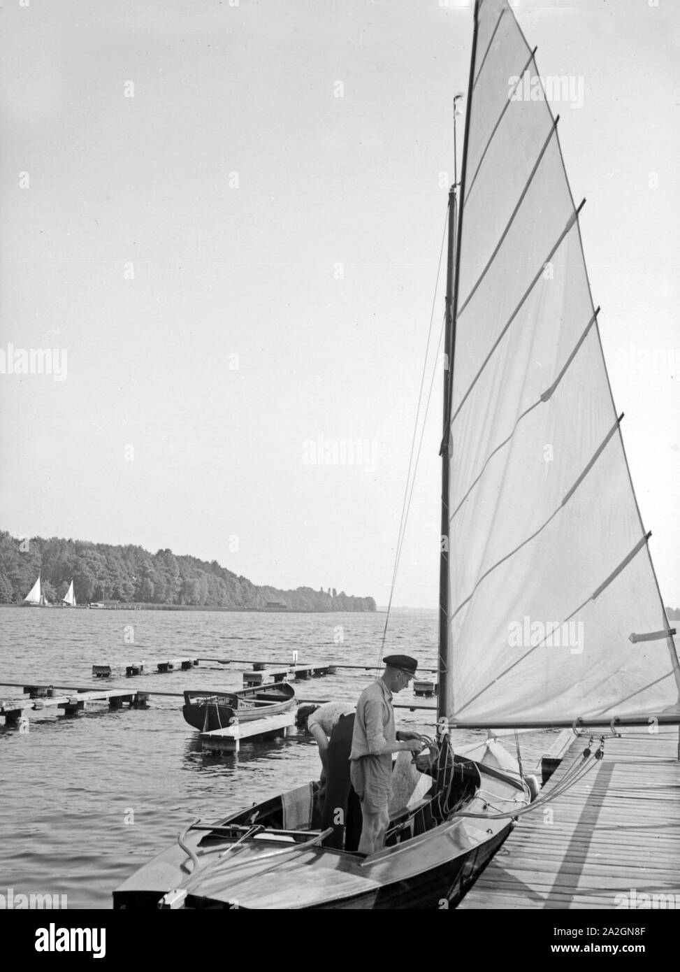 Ein Segelboot beim Anlegen un einem Holzsteg am Ufer eines vede, Deutschland 1930er Jahre. Una barca a vela l'ancoraggio ad una boarwalk sulla riva di un lago, Germania 1930s. Foto Stock