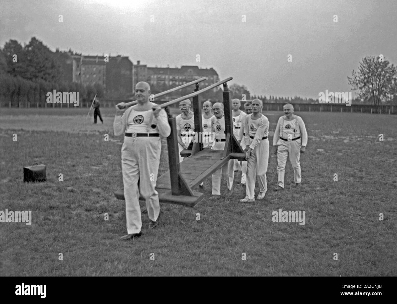 Die Altherrenriege eines Turnvereins trägt einen Stufenbarren über einen Sportplatz, Deutschland 1930er Jahre. Dipartimento senior di un club ginnico che trasportano le barre irregolari su un terreno sportivo, Germania 1930s. Foto Stock