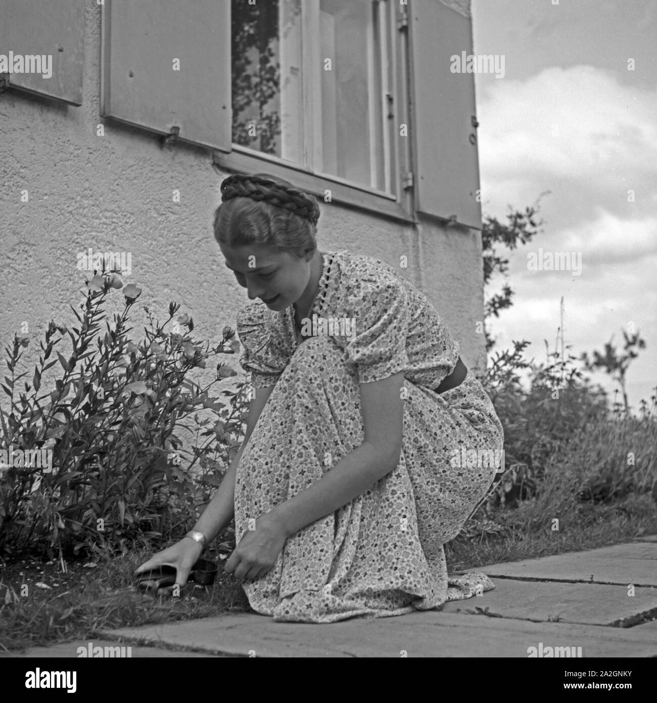 Eine junge Frau beim Unkrautjäten im Vorgarten, Deutschland 1930er Jahre. Una giovane donna weeding presso il suo giardino, Germania 1930s. Foto Stock