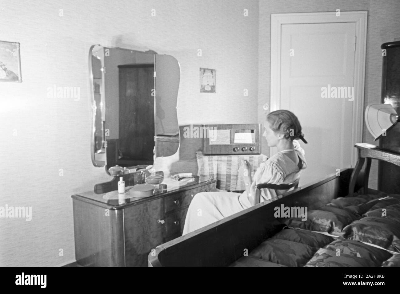 Eine Frau sitzt am Frisiertisch und hört Radio, Deutschland 1930er Jahre. Una donna seduta al tavolo mentre si ascolta la radio, Germania 1930s. Foto Stock