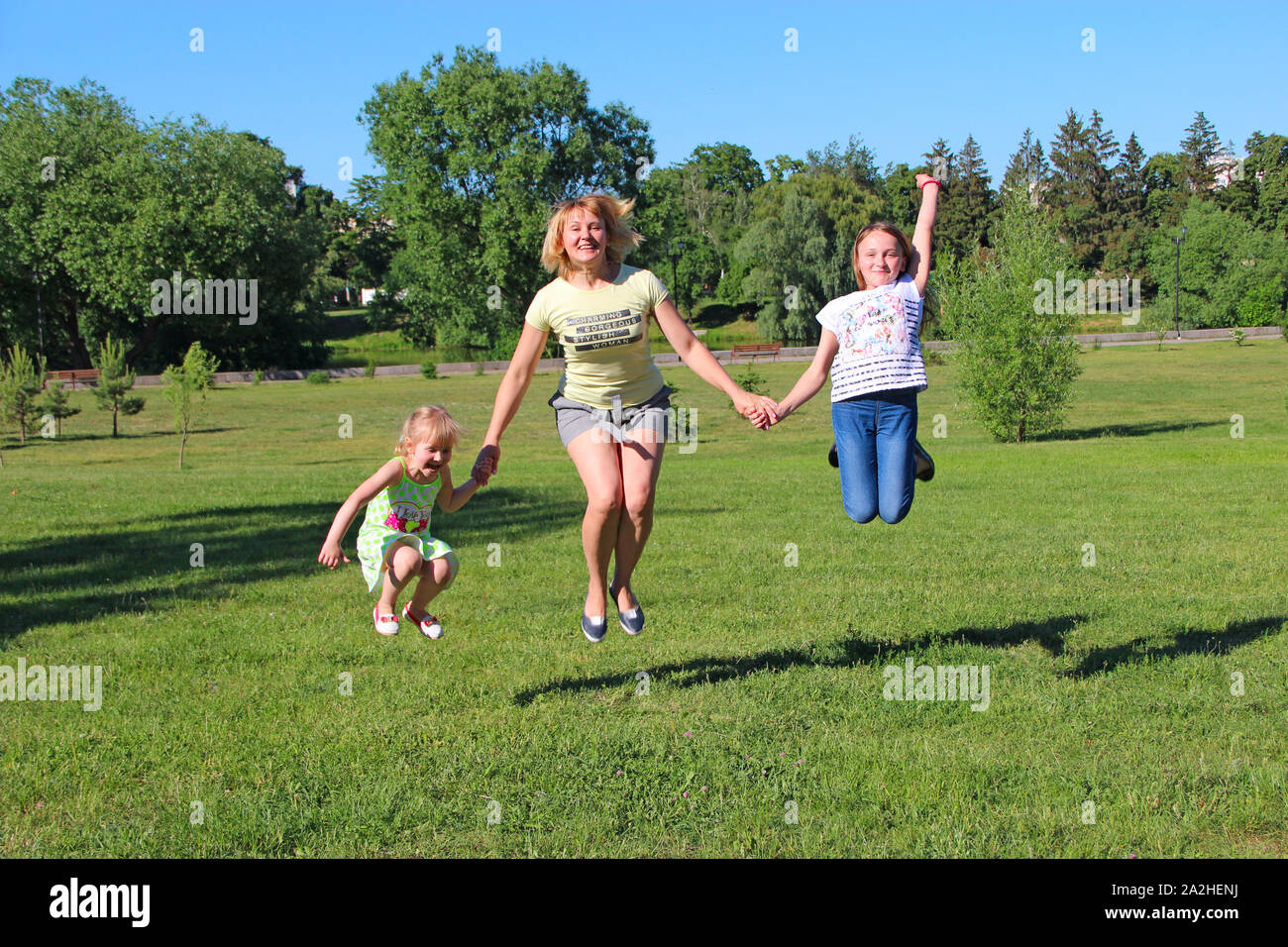 Felice madre divertirsi saltando con le sue figlie sull'erba verde. La famiglia felice team. Famiglia godendo le vacanze estive. Le persone che si godono la vacanza con la famiglia Foto Stock