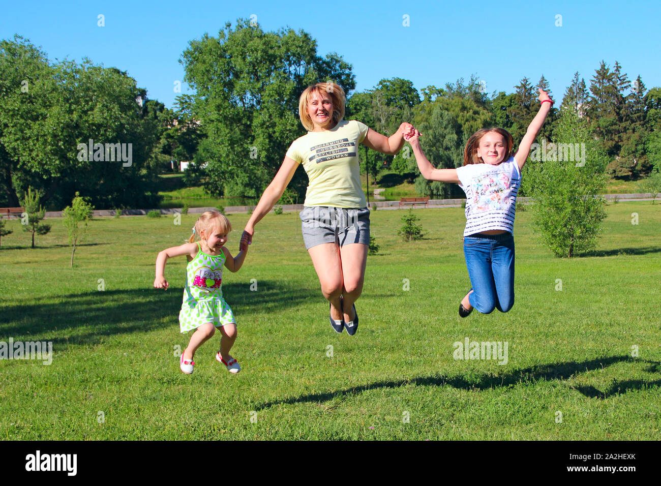 Felice madre divertirsi saltando con le sue figlie sull'erba verde. La famiglia felice team. Famiglia godendo le vacanze estive. Le persone che si godono la vacanza con la famiglia Foto Stock