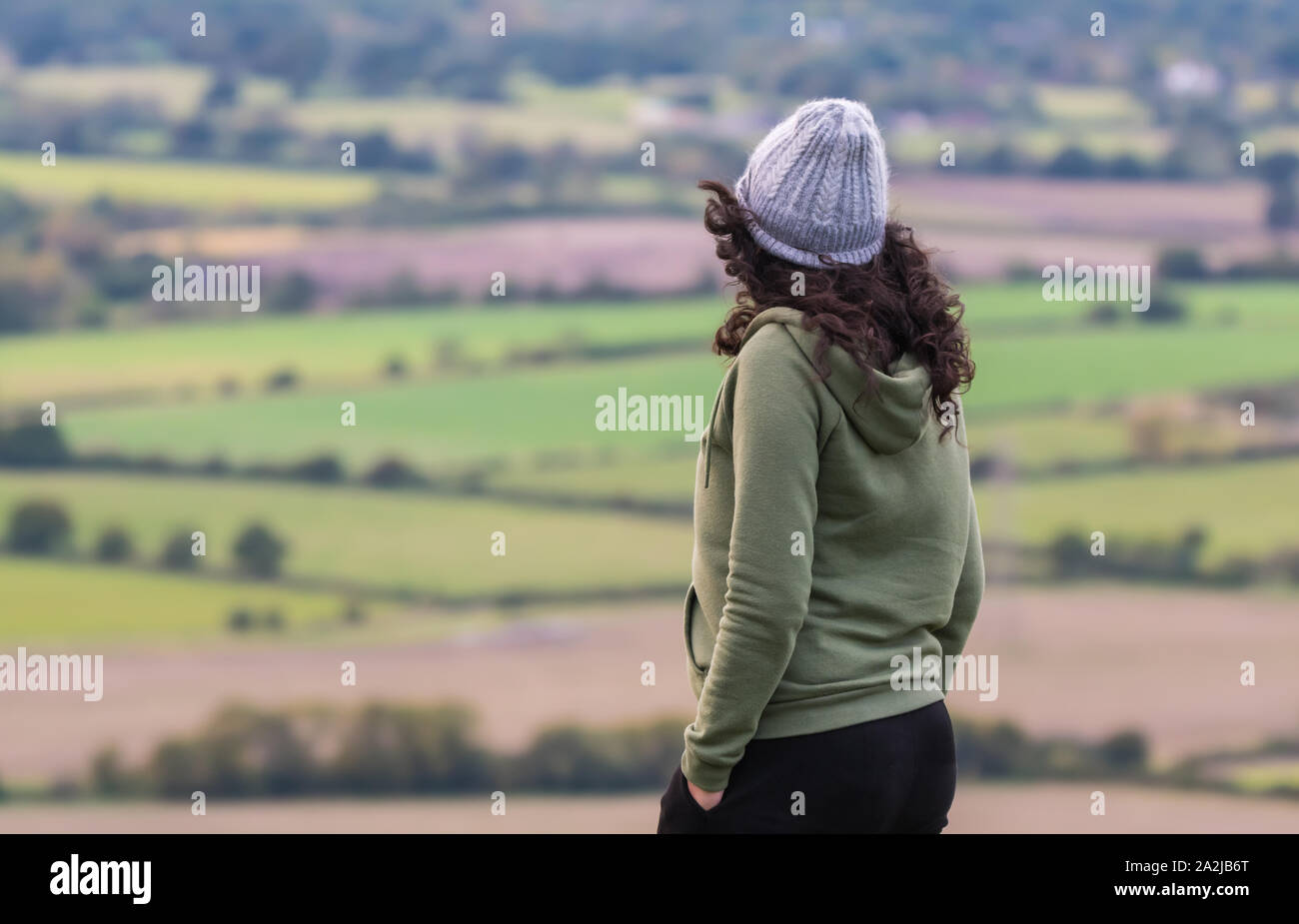 Giovane donna che indossa un cappello e il ponticello facendo una passeggiata serale nel tempo ventoso nel South Downs e colline del West Sussex, in Inghilterra, Regno Unito. Foto Stock