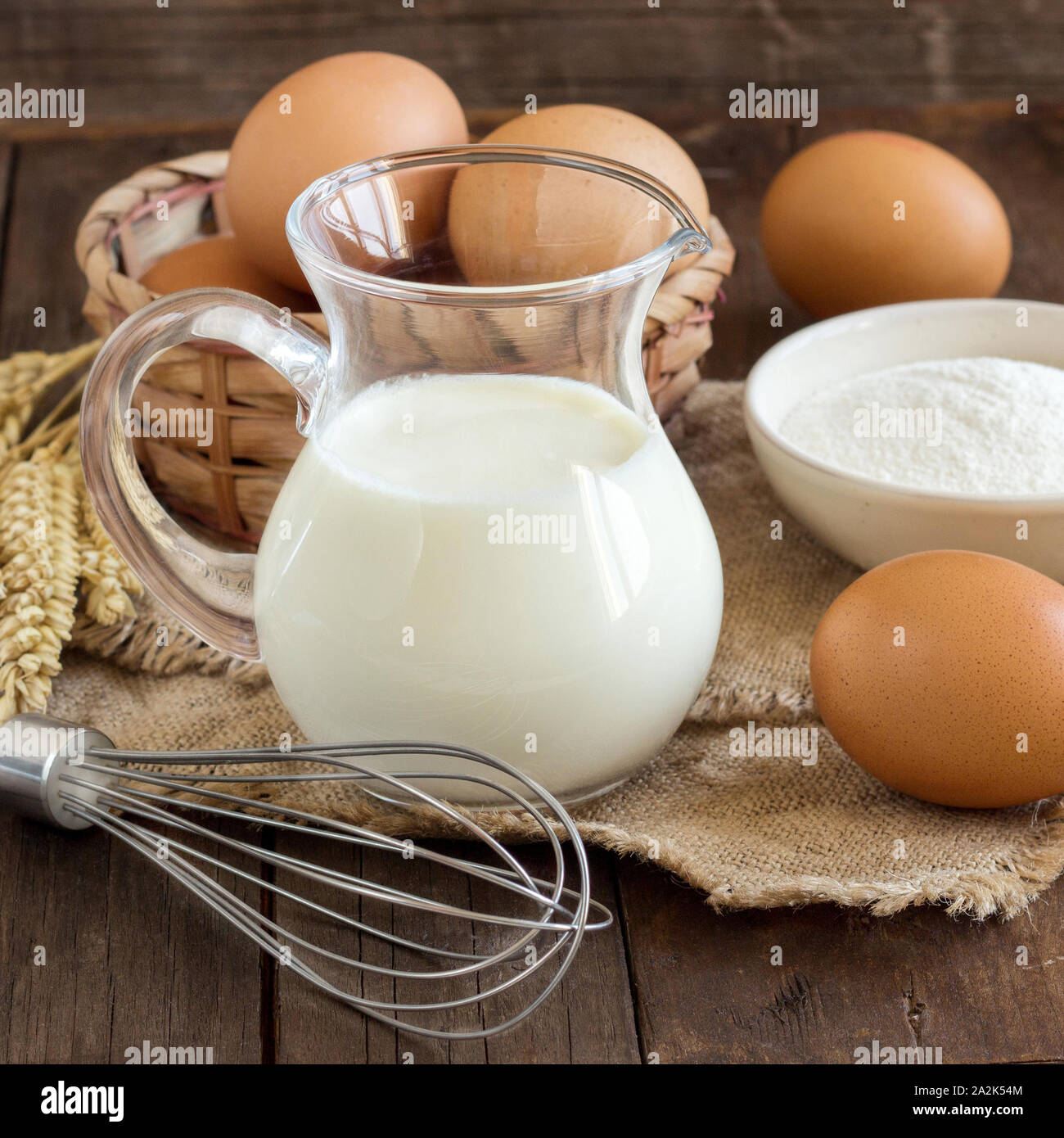 Il latte, la farina di frumento, frusta e uova sul vecchio tavolo in legno Foto Stock