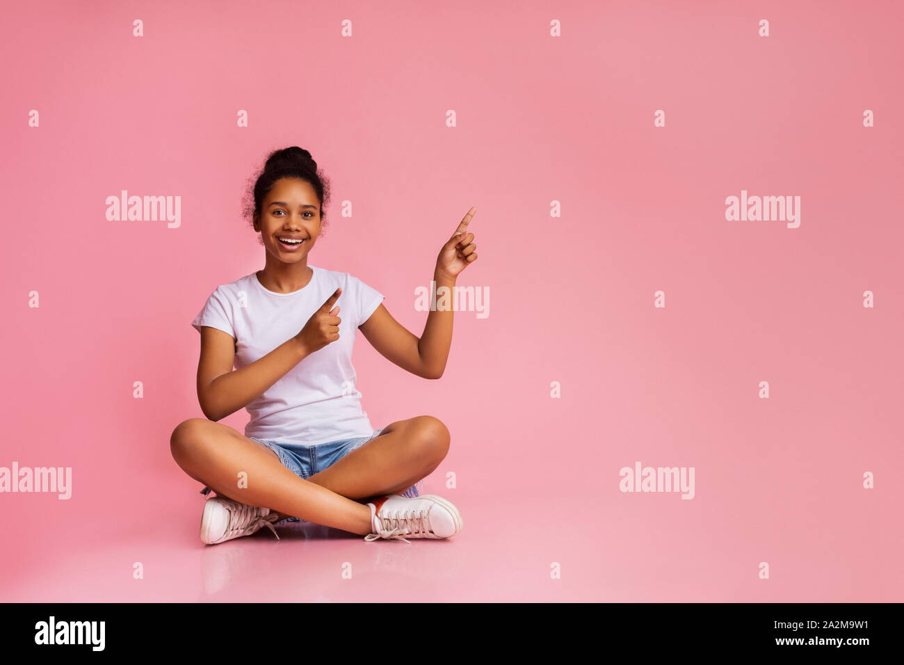 Felice ragazza seduta con le gambe incrociate e denti rivolti verso l'alto Foto Stock