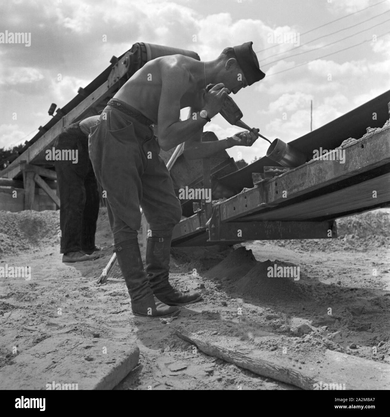 Original-Bildunterschrift: Reichsautobahnzubringer Berlino - Polnischer Gefangener beim Ölen eines Transportbandes zur Fertigstellung des Zubringers während des Krieges. Motore feeder a Reichsautobahn autostrada - Polacco prigioniero di guerra di olio di lubrificazione di un nastro trasportatore per la zona di costruzione in attraversamento di Wannsee e Potsdamer Chaussee, Germania 1940. Foto Stock