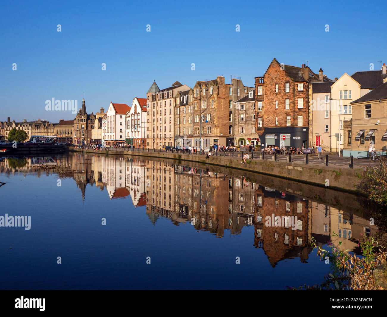 Edifici antichi lungo la riva riflessa nell'acqua di Leith in una serata estiva Leith città di Edimburgo in Scozia Foto Stock