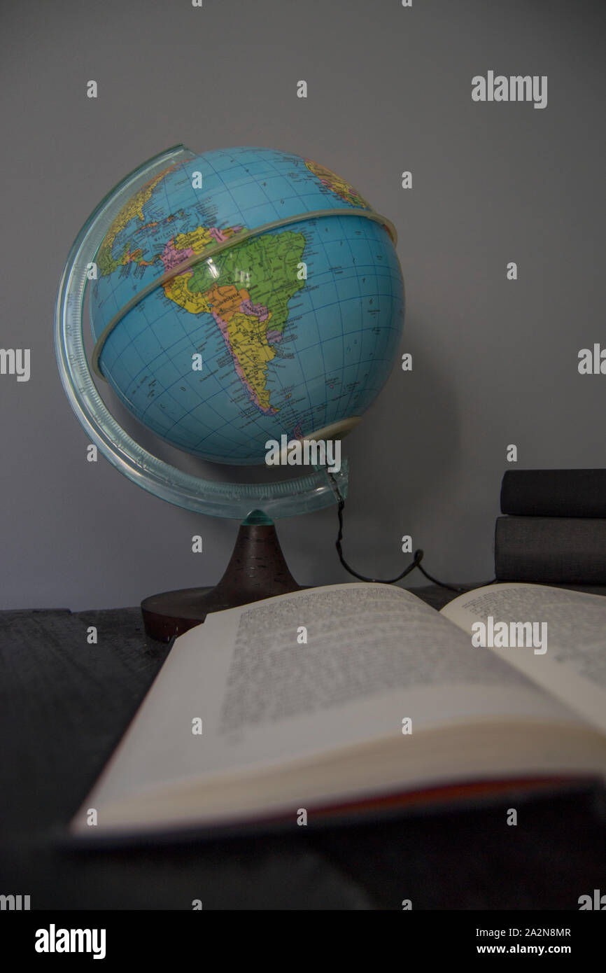 Sfera di terra con libri su sfondo grigio Foto Stock
