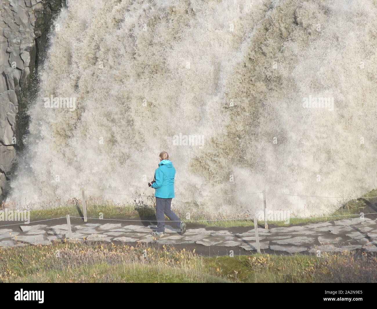 Un turista solitario sul sentiero in pietra è sopraffatte da la scala e il volume di acqua a Dettifoss, Islanda la più grande cascata. Foto Stock